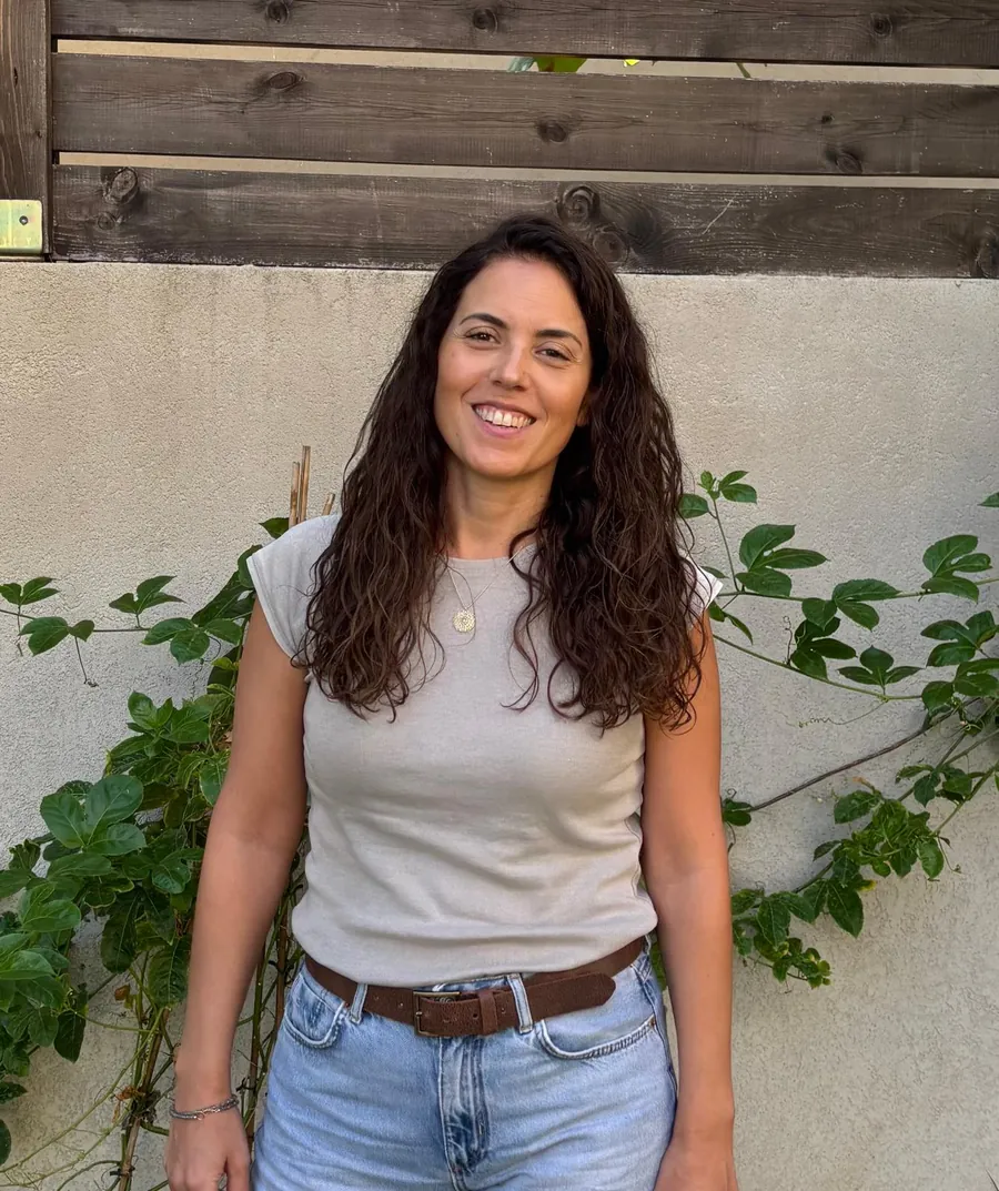 דליה שני ברייר, יועצת ומלווה עסקית, עומדת בחוץ ליד קיר עם צמחייה ומחייכת